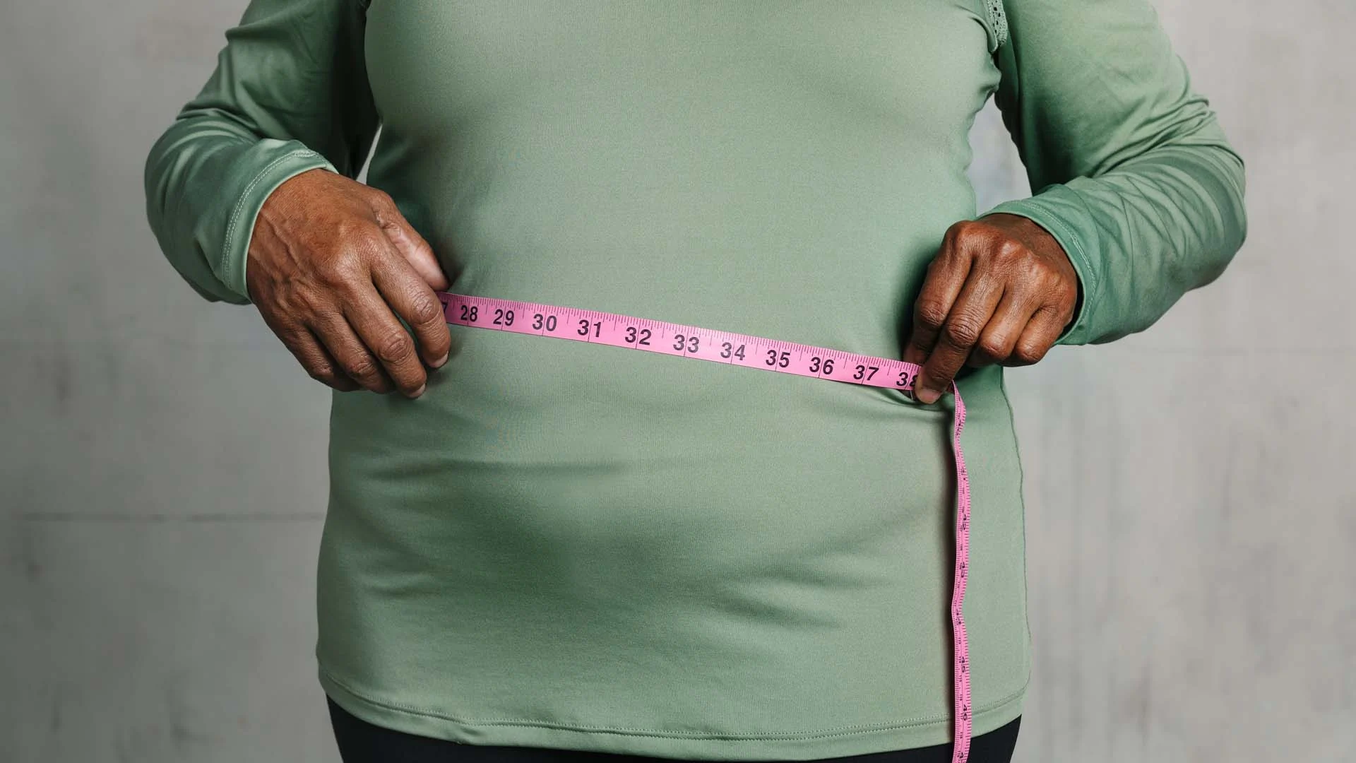 Femme ménopausée mesurant son tour de taille devant un miroir pour évaluer sa prise de poids.